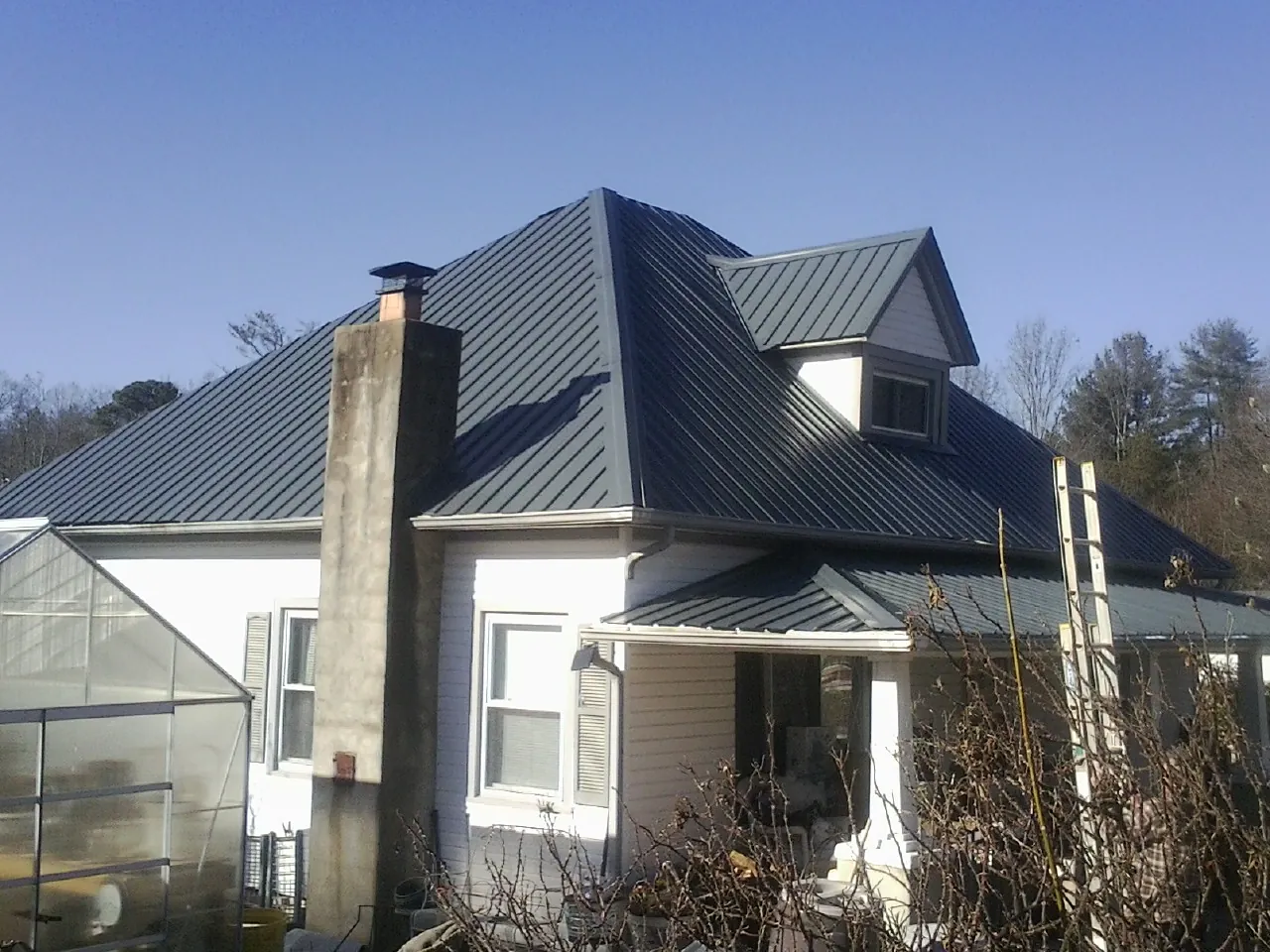 Dark blue standing seam metal roof on a white farmhouse with dormer — Slate & Tile Roof Repair by Roofing Brothers in Laclede