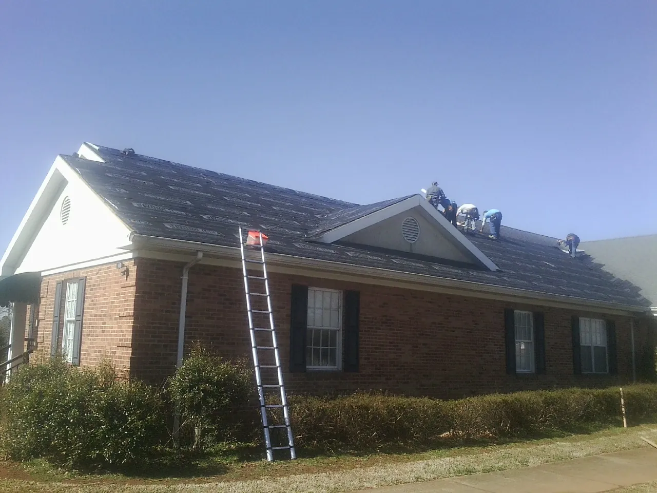Crew tearing shingles off a brick ranch roof with a ladder set — Emergency Roof Repair work by our crew in Laclede
