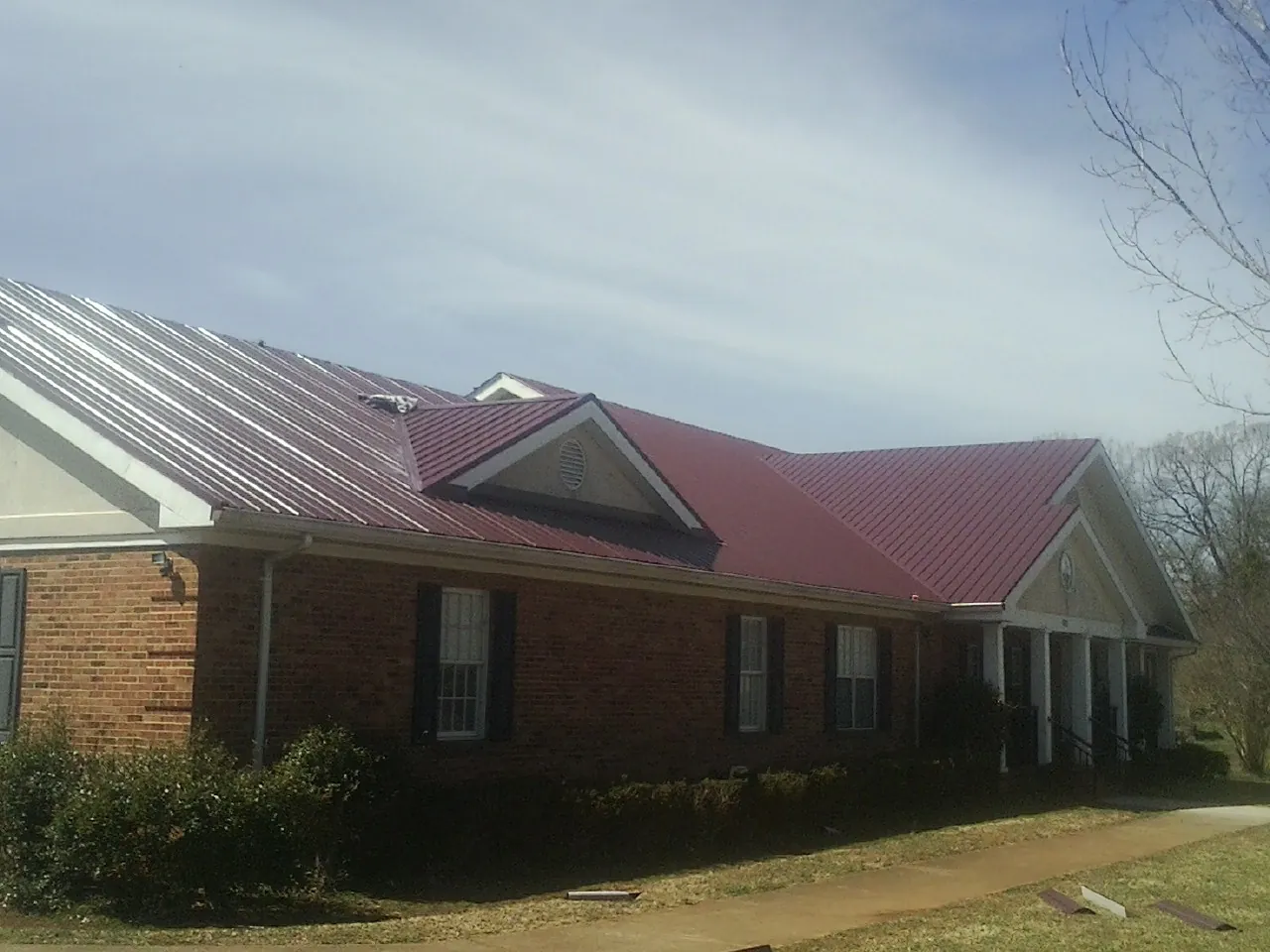 Red metal roof with gabled entries on a long brick building, from a Hail Damage Roof Repair job in Laclede