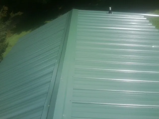New green metal panels meeting at the ridge of a roof — Flat Roof Repair work by our crew in Laclede