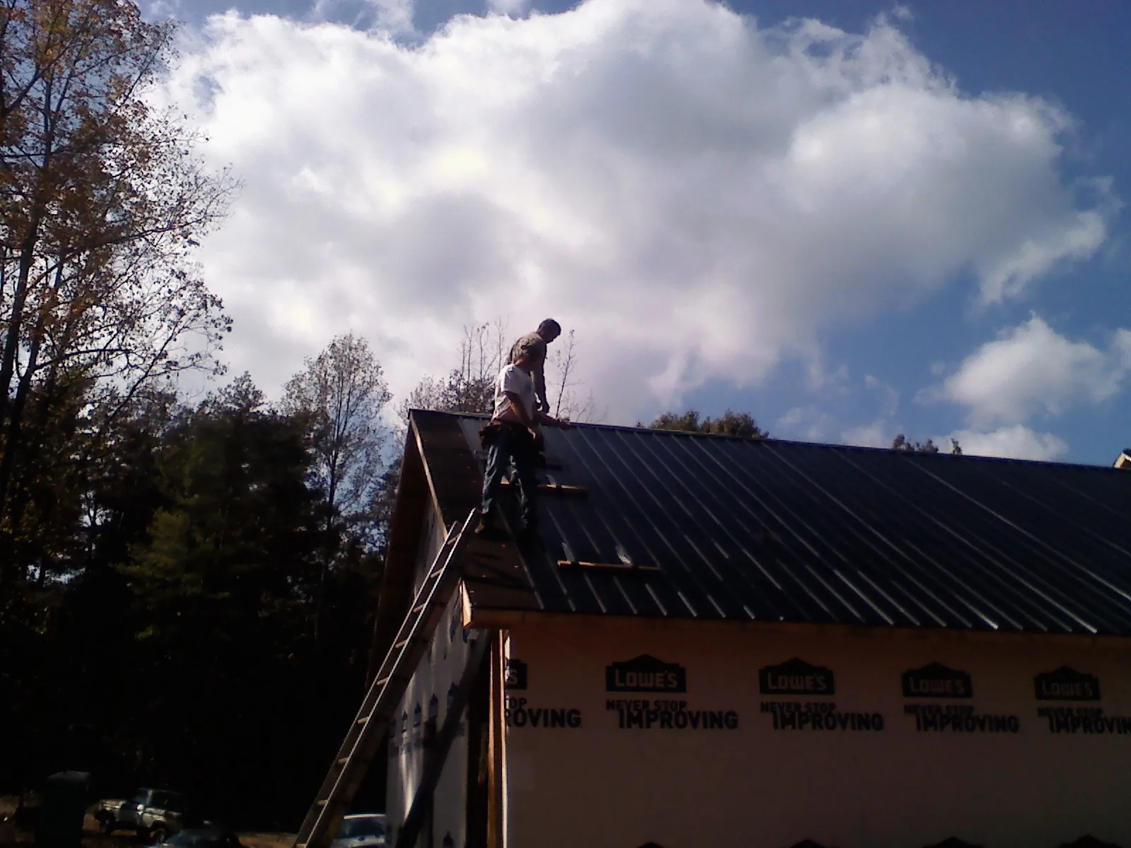 Roofer fastening dark metal panels high against a cloudy sky, from a Roof Inspection job in Laclede